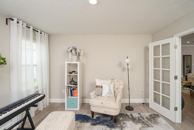 sitting room with a textured ceiling, baseboards, and wood finished floors