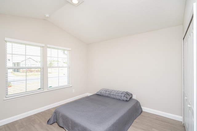 bedroom featuring lofted ceiling, a closet, baseboards, and light wood-style floors