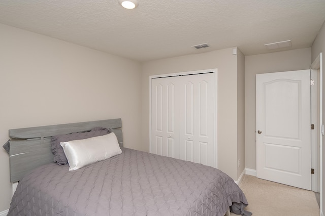 carpeted bedroom with a textured ceiling, a closet, visible vents, and baseboards