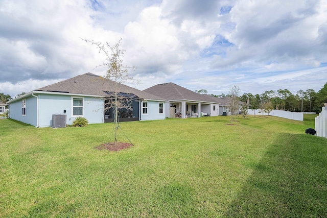 back of property with a lawn, fence, central AC unit, and stucco siding