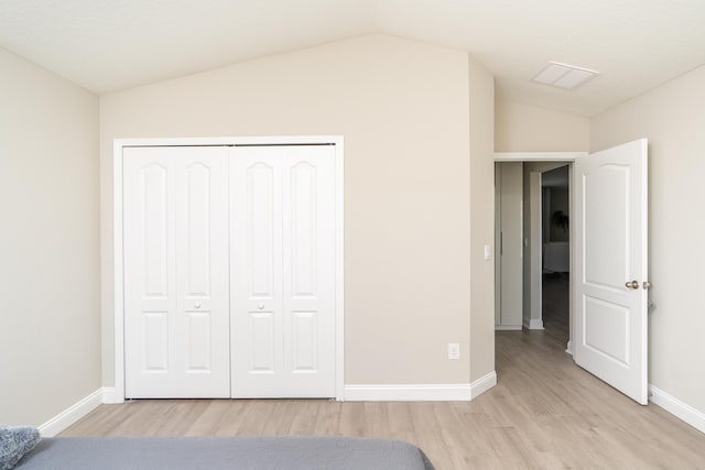 unfurnished bedroom featuring a closet, vaulted ceiling, light wood-style flooring, and baseboards