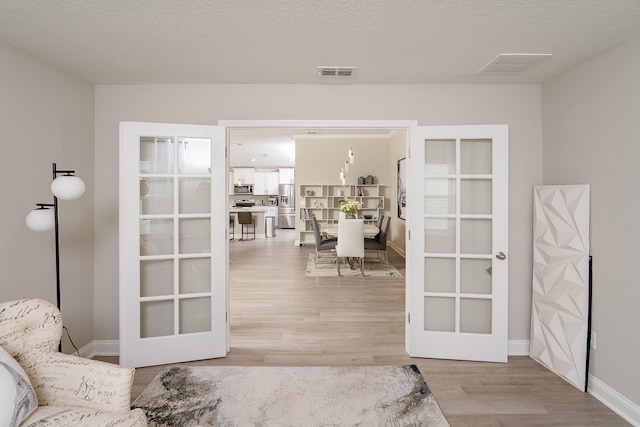 interior space featuring a textured ceiling, french doors, wood finished floors, and visible vents