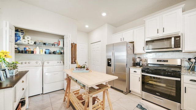 kitchen with white cabinets, stainless steel appliances, washing machine and dryer, and light tile patterned floors