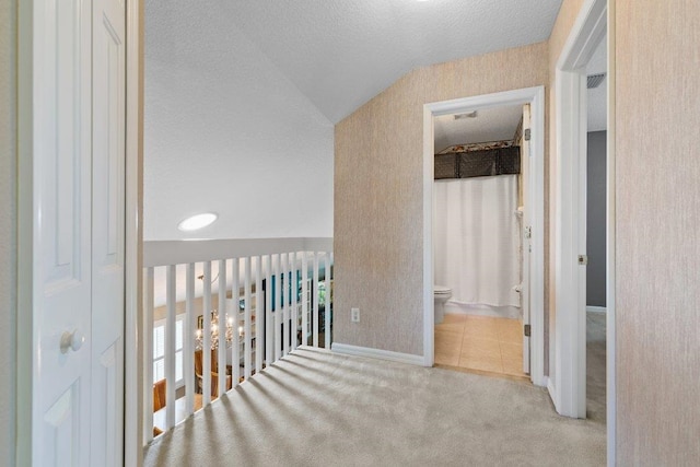 hall featuring a textured ceiling, tile patterned flooring, baseboards, lofted ceiling, and carpet