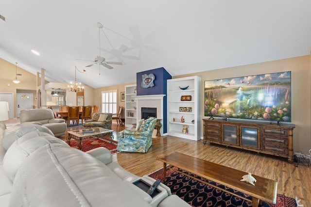 living area with ceiling fan with notable chandelier, wood finished floors, lofted ceiling, and a fireplace