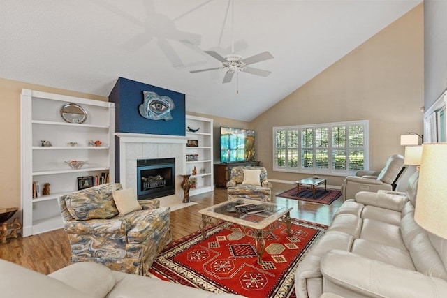 living area with high vaulted ceiling, ceiling fan, wood finished floors, and a tile fireplace