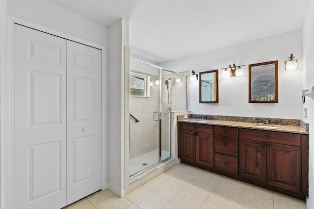 full bathroom with a sink, a textured ceiling, a shower stall, and double vanity