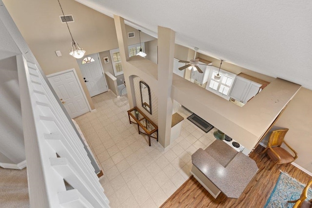 entrance foyer with visible vents, baseboards, ceiling fan with notable chandelier, and high vaulted ceiling