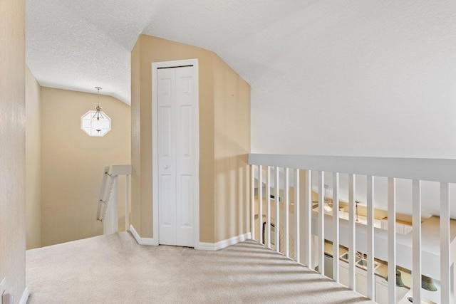 corridor with lofted ceiling, baseboards, a textured ceiling, carpet flooring, and an upstairs landing
