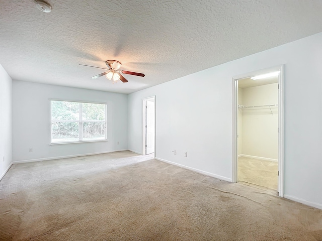 unfurnished bedroom featuring a walk in closet, ceiling fan, light colored carpet, and a textured ceiling