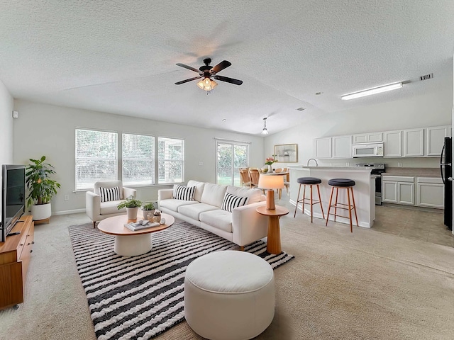 living room with a textured ceiling, ceiling fan, light carpet, and vaulted ceiling