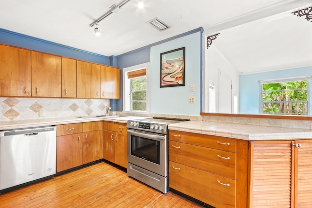 26 Ponce De Leon Ave, Saint Augustine, FL 32080 - kitchen with stainless steel appliances, light wood-style flooring, brown cabinetry, rail lighting, and decorative backsplash