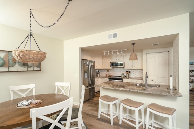 kitchen with appliances with stainless steel finishes, pendant lighting, tasteful backsplash, sink, and light stone countertops