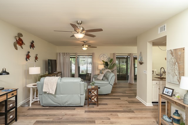 living room featuring ceiling fan, sink, and light wood-type flooring