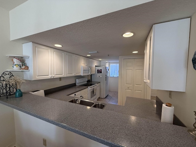 kitchen with sink, kitchen peninsula, a textured ceiling, white appliances, and white cabinets