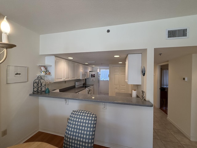 kitchen featuring kitchen peninsula, a breakfast bar, white appliances, white cabinets, and light tile patterned flooring