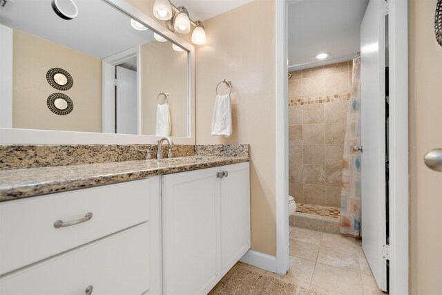 bathroom featuring toilet, tile patterned flooring, vanity, and tiled shower