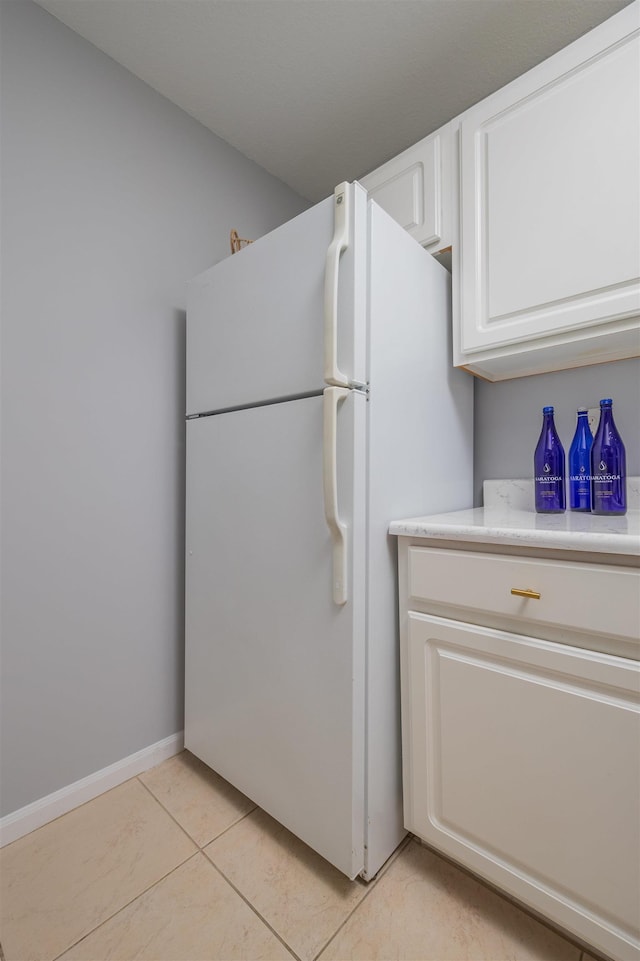 kitchen featuring white refrigerator, light tile patterned flooring, and white cabinets