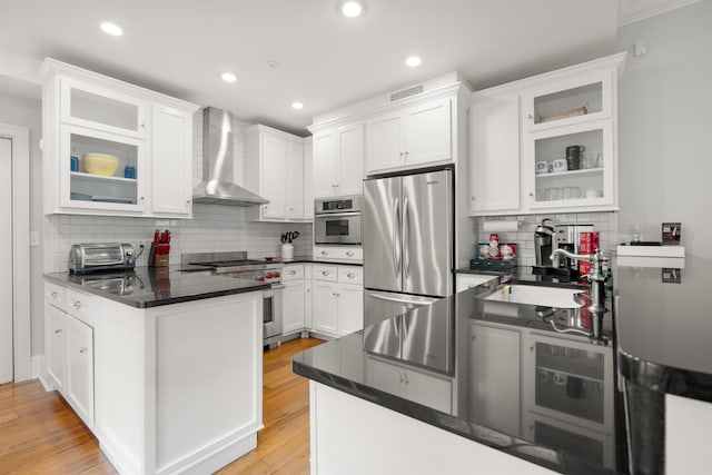 kitchen with backsplash, white cabinets, wall chimney range hood, light wood-type flooring, and appliances with stainless steel finishes