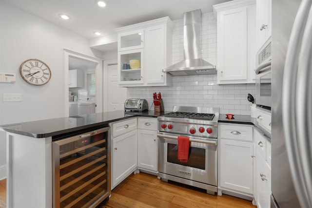 kitchen featuring appliances with stainless steel finishes, wall chimney exhaust hood, beverage cooler, light hardwood / wood-style flooring, and white cabinetry