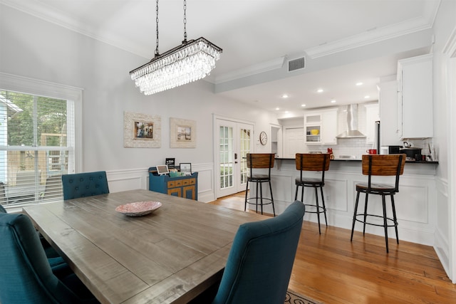 dining space with a notable chandelier, light hardwood / wood-style flooring, french doors, and ornamental molding