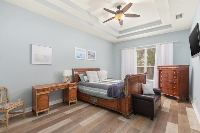 bedroom with light hardwood / wood-style floors, ceiling fan, and a raised ceiling