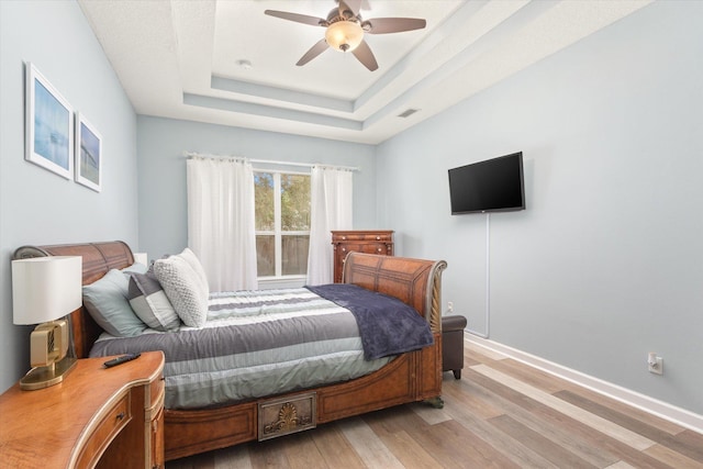 bedroom with ceiling fan, a tray ceiling, and light hardwood / wood-style flooring