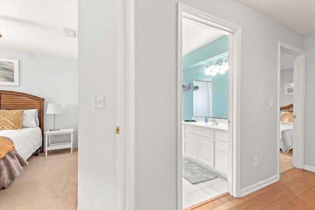 bedroom featuring sink, light hardwood / wood-style floors, a textured ceiling, and ensuite bath