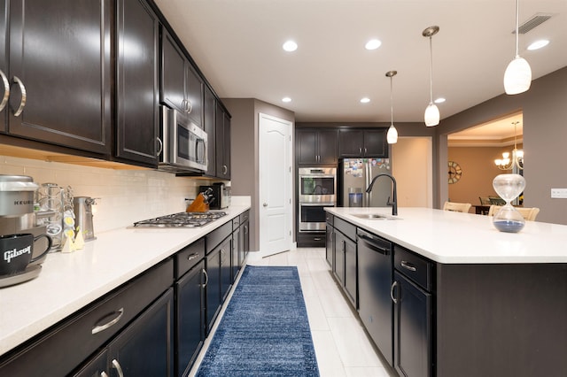 kitchen with backsplash, a kitchen island with sink, hanging light fixtures, light tile patterned flooring, and stainless steel appliances