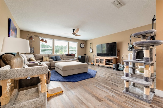 living room featuring wood-type flooring, a textured ceiling, and ceiling fan