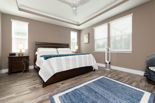 bedroom featuring ceiling fan, wood-type flooring, ornamental molding, and a tray ceiling