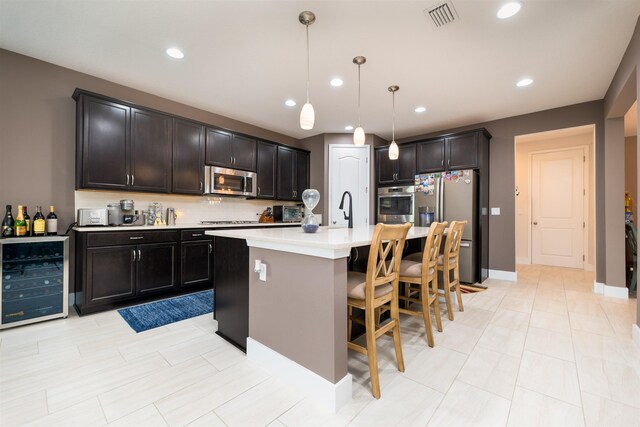 kitchen with hanging light fixtures, beverage cooler, stainless steel appliances, a breakfast bar, and a center island with sink