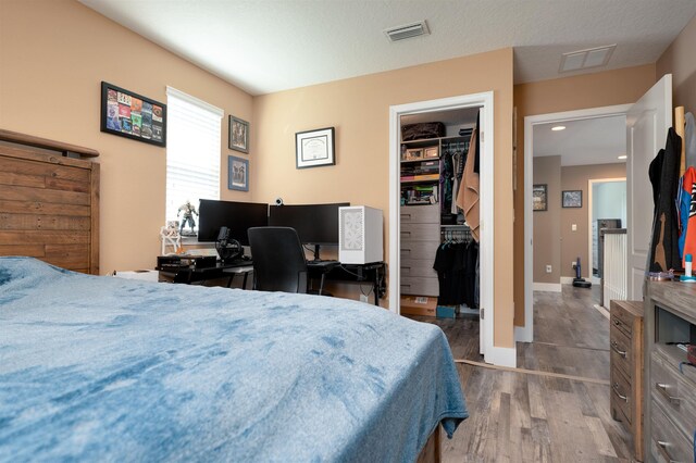 bedroom with a textured ceiling, dark hardwood / wood-style floors, a spacious closet, and a closet