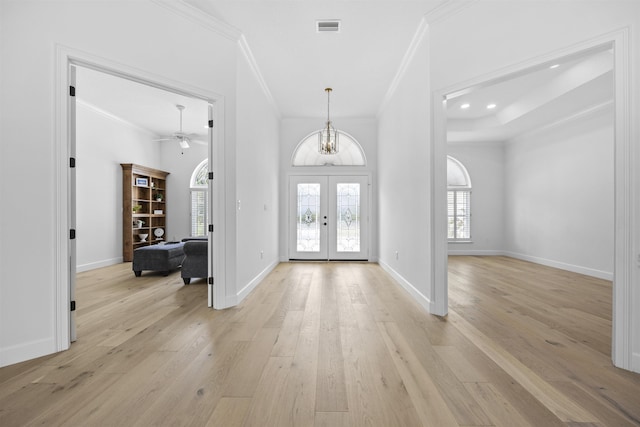 foyer entrance with an inviting chandelier, crown molding, light hardwood / wood-style flooring, and french doors