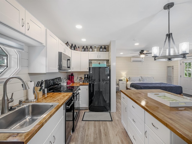 kitchen with butcher block counters, pendant lighting, white cabinets, and black appliances