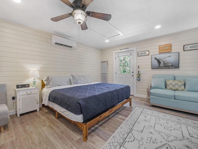 bedroom featuring light hardwood / wood-style floors, a wall unit AC, ceiling fan, and wood walls