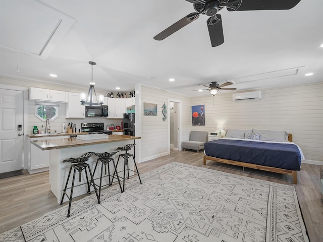 bedroom featuring a wall mounted air conditioner, black fridge, light wood-type flooring, and sink