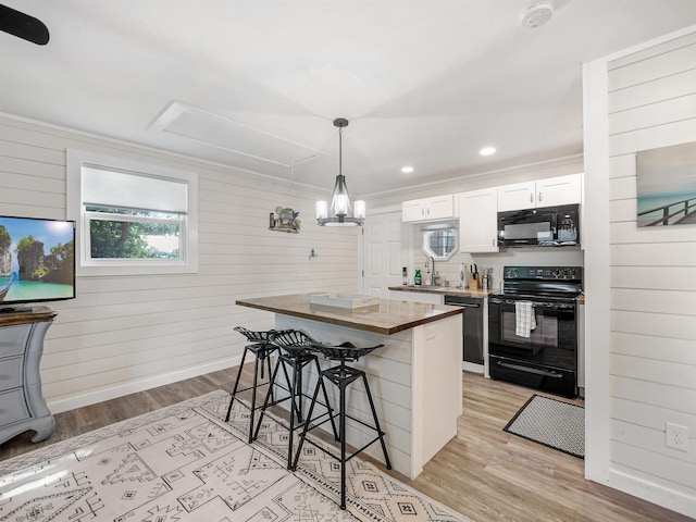 kitchen featuring a center island, hanging light fixtures, a breakfast bar, white cabinets, and black appliances