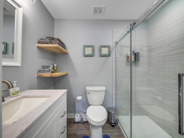 bathroom featuring hardwood / wood-style floors, a textured ceiling, an enclosed shower, toilet, and vanity