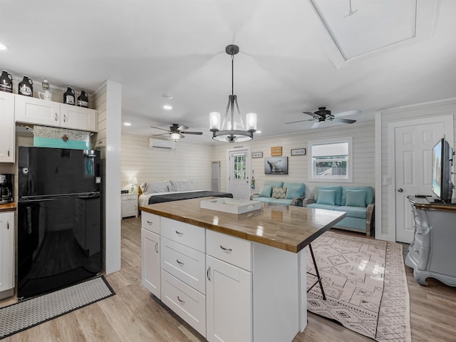 kitchen with a center island, black refrigerator, decorative light fixtures, white cabinetry, and butcher block counters