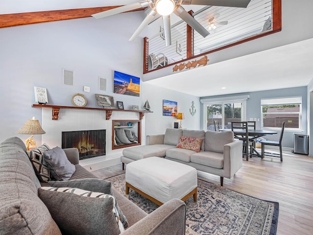 living room featuring beam ceiling, ceiling fan, high vaulted ceiling, light hardwood / wood-style floors, and a fireplace