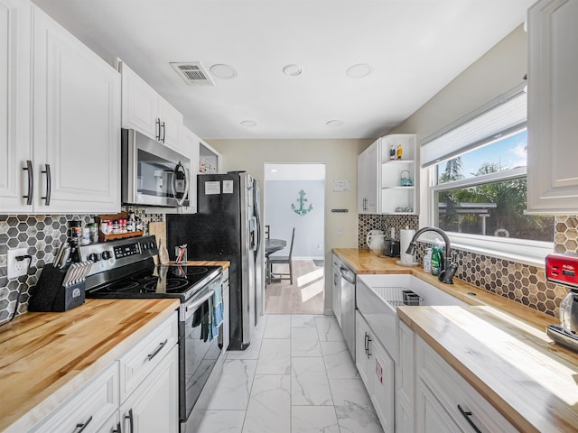 kitchen with wood counters, appliances with stainless steel finishes, decorative backsplash, and white cabinetry