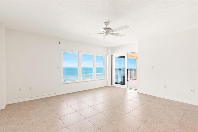 tiled empty room with ceiling fan, a water view, and a textured ceiling