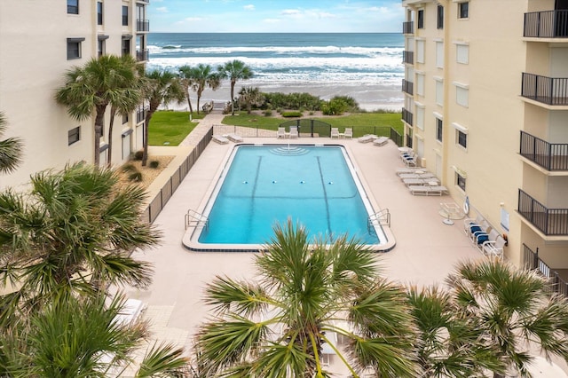 view of pool featuring a patio area, a water view, and a beach view