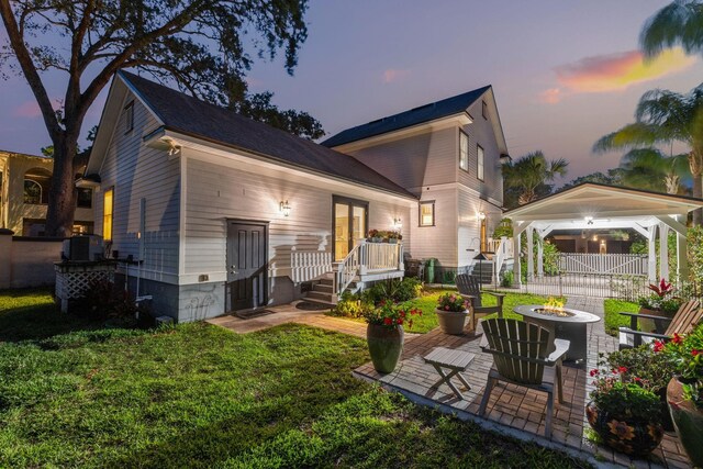 back house at dusk with central AC, a fire pit, a patio area, and a lawn