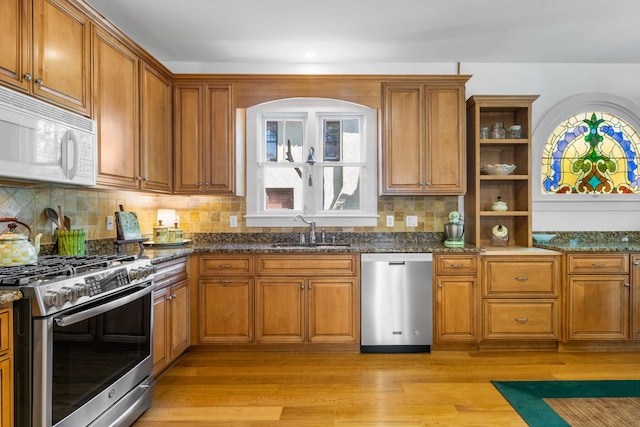 kitchen featuring decorative backsplash, light wood-type flooring, dark stone counters, stainless steel appliances, and sink