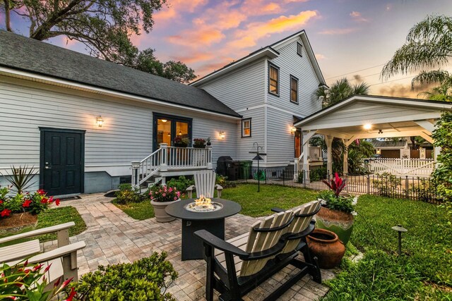 back house at dusk with a fire pit, a patio area, and a lawn