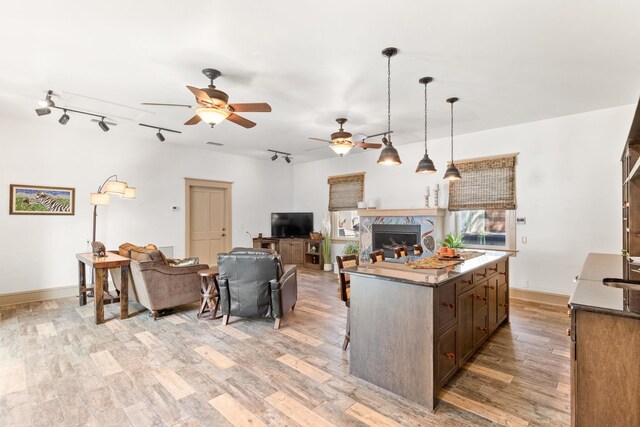 kitchen with dark brown cabinetry, ceiling fan, pendant lighting, light hardwood / wood-style floors, and a kitchen island