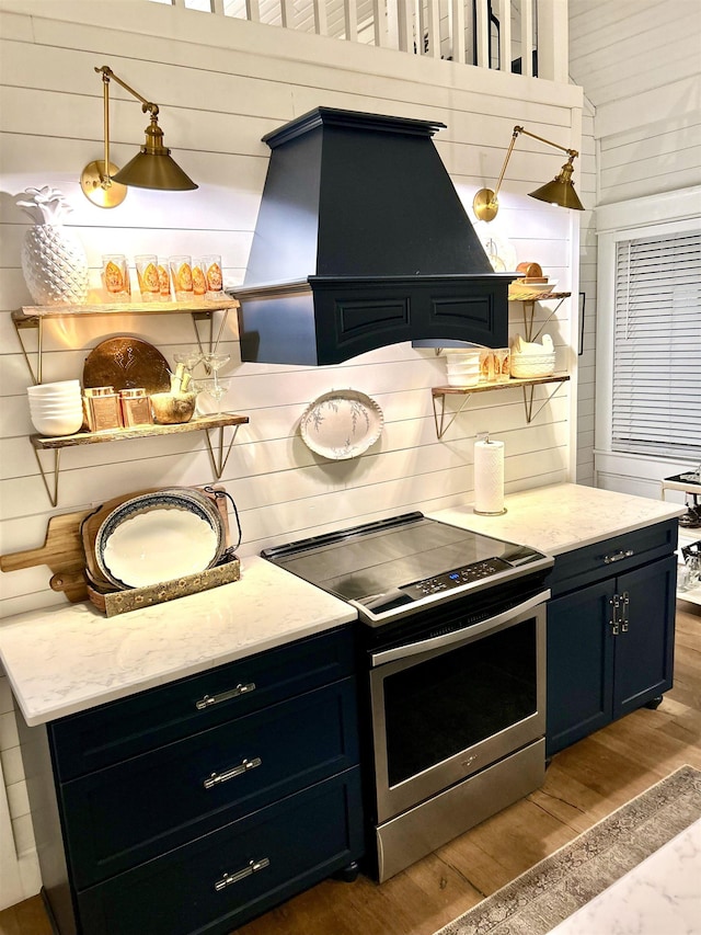 kitchen with stainless steel electric stove, wood walls, custom range hood, and hardwood / wood-style floors