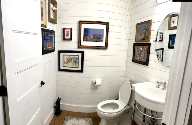 bathroom featuring hardwood / wood-style floors, toilet, wood walls, and sink